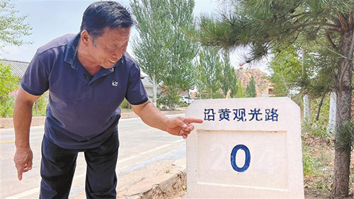 王清玉指着界碑介绍这条路给墙头村带来的巨大变化.jpg
